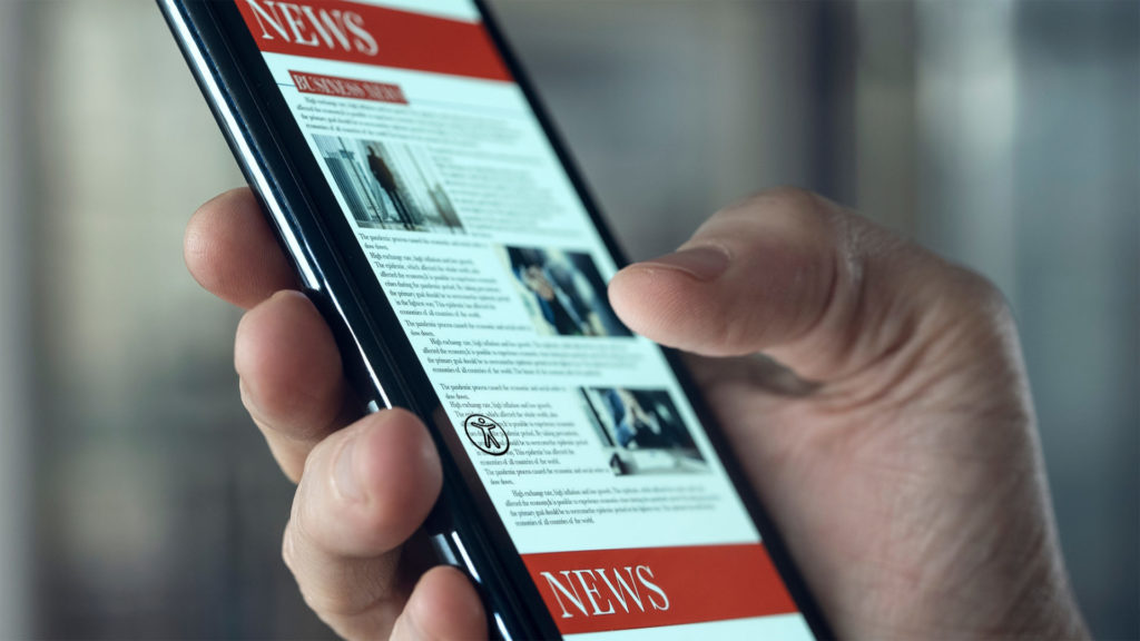 Hand holding a mobile phone with the accessibility overlay icon on lower left.