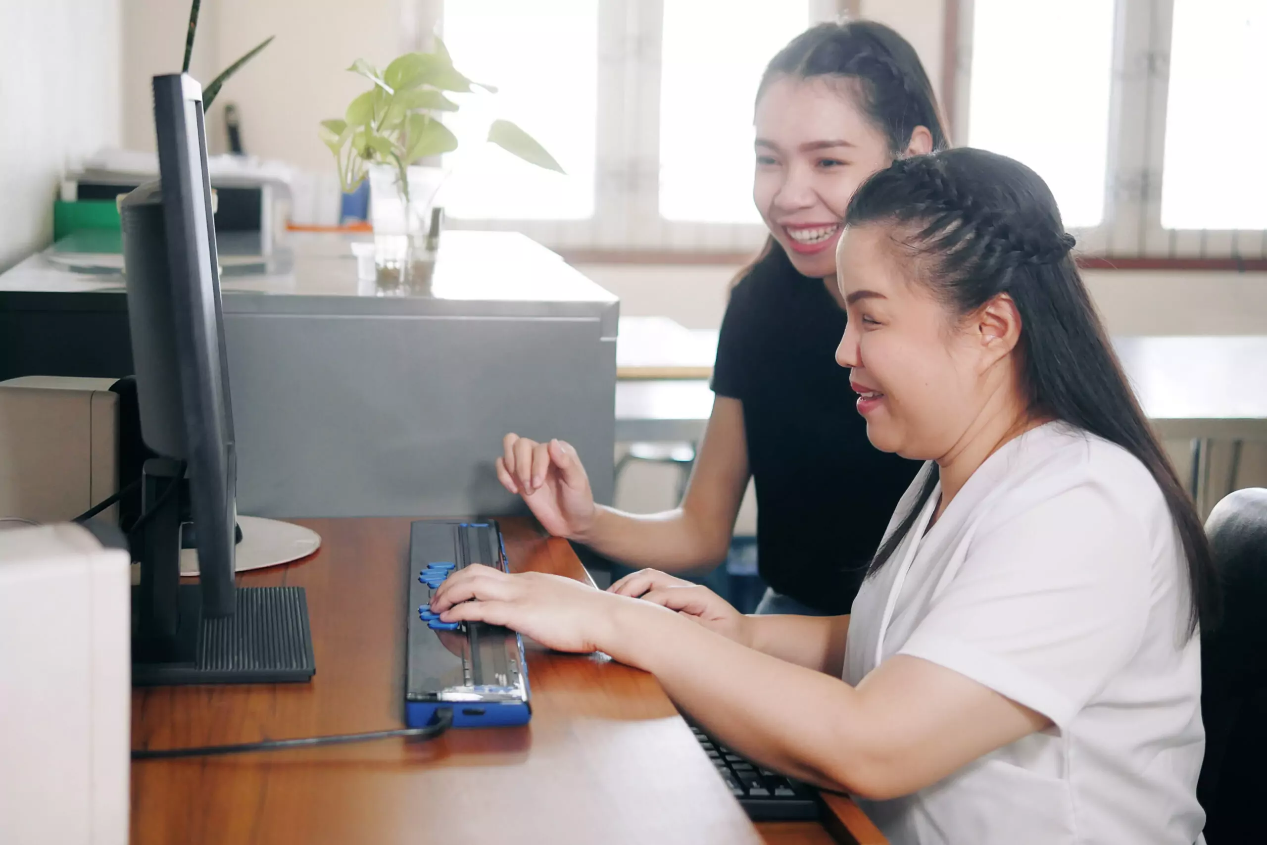 A woman with blindness disability using computer with braille display assistive device.