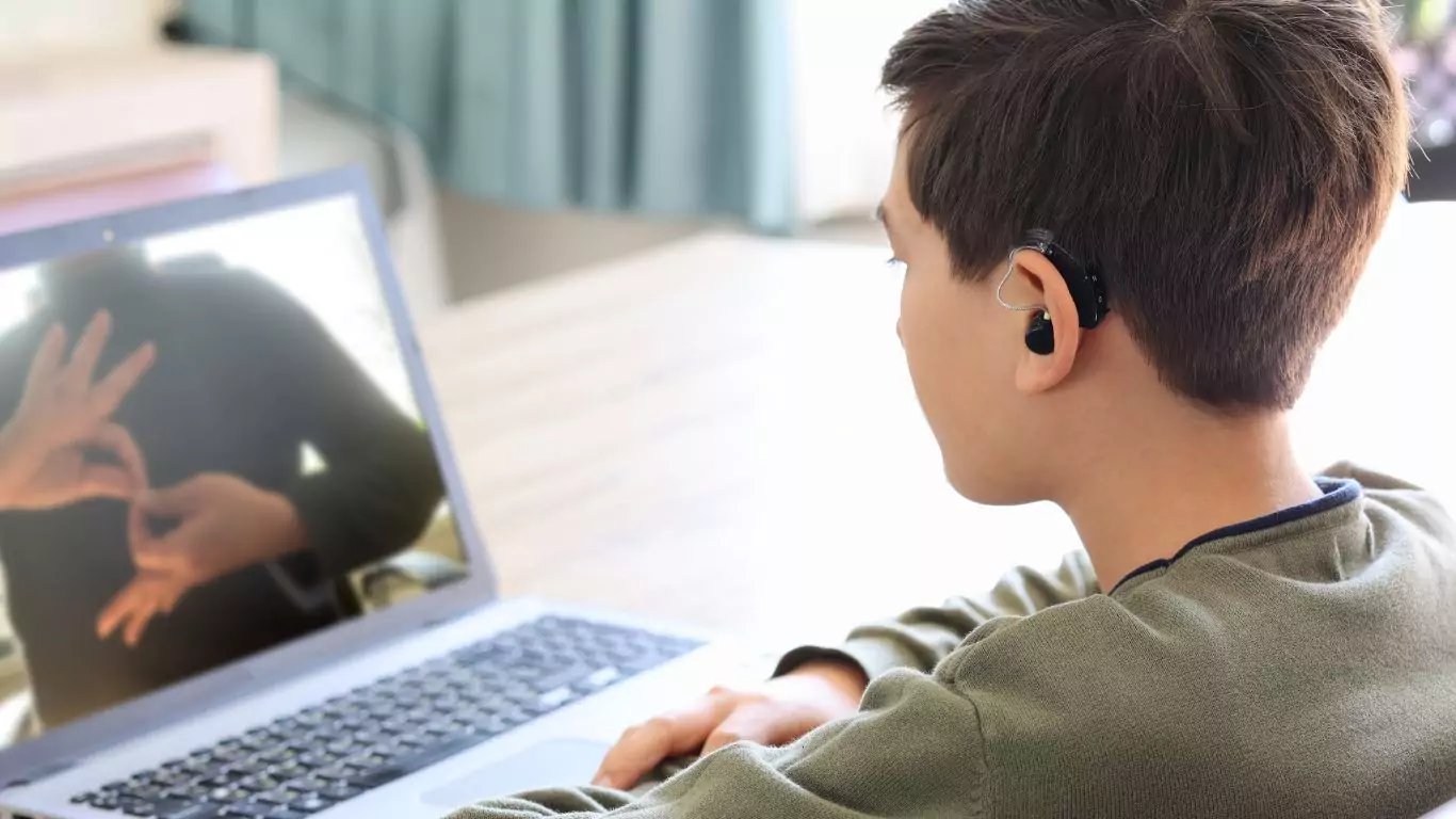 Teenager boy wearing hearing aid using laptop