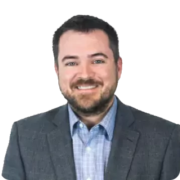 White male with short dark hair and a beard. Smiling, he is wearing a grey sport coat and light blue shirt.