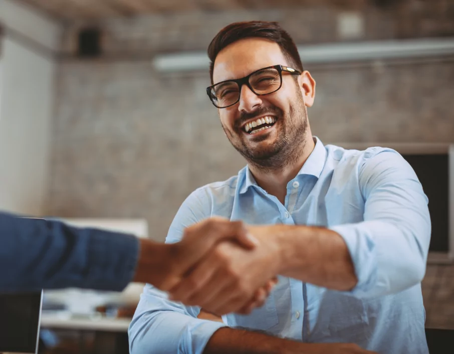 A man smiling while shaking someone's hand.