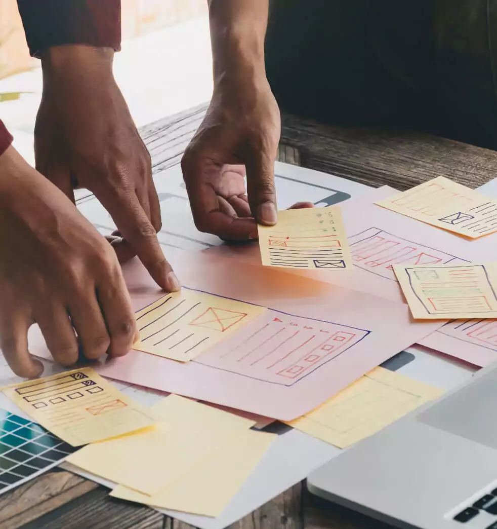 Two people are standing around a table, pointing out black and white mockups.