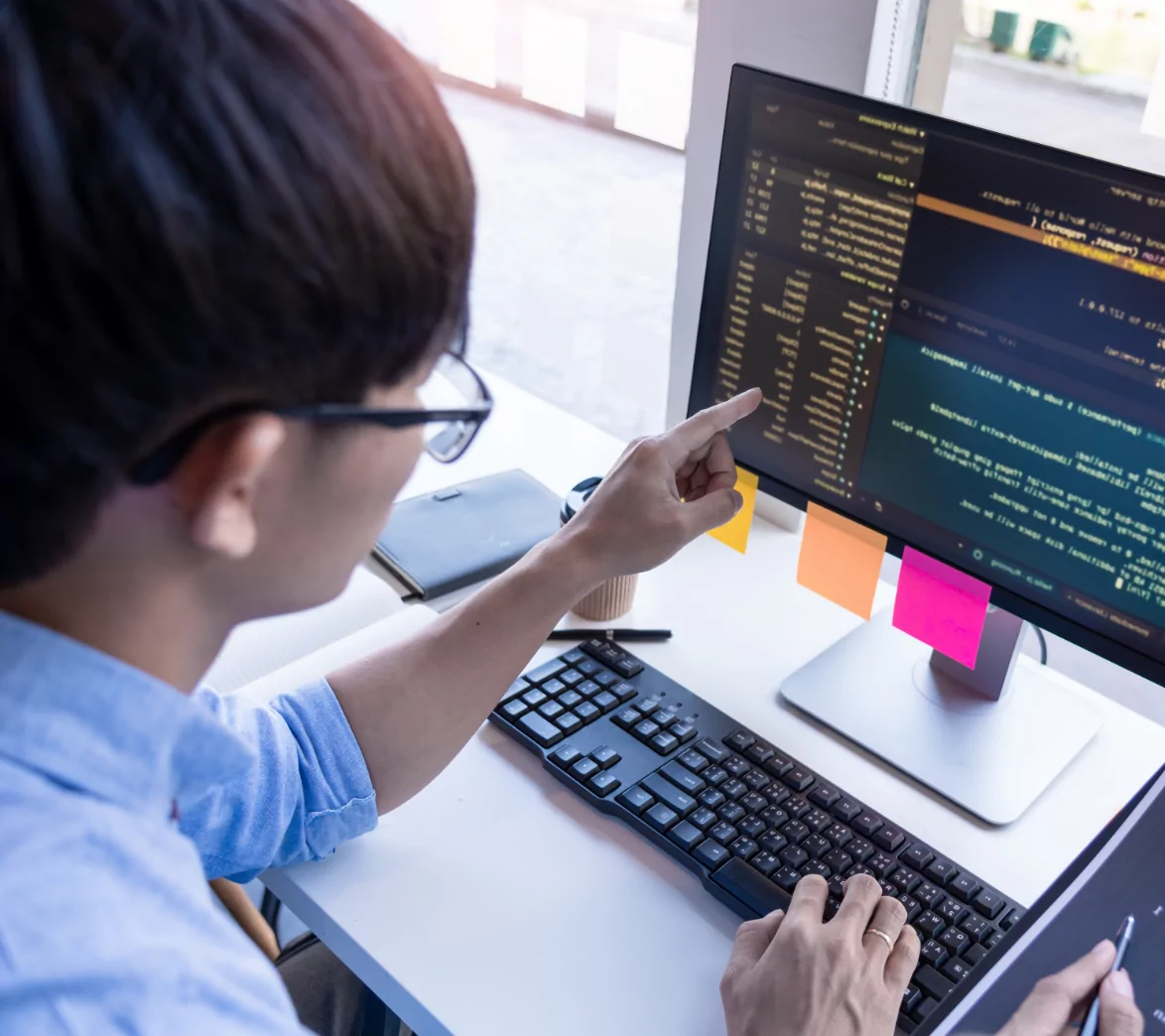 A man pointing to code displayed on a computer monitor.
