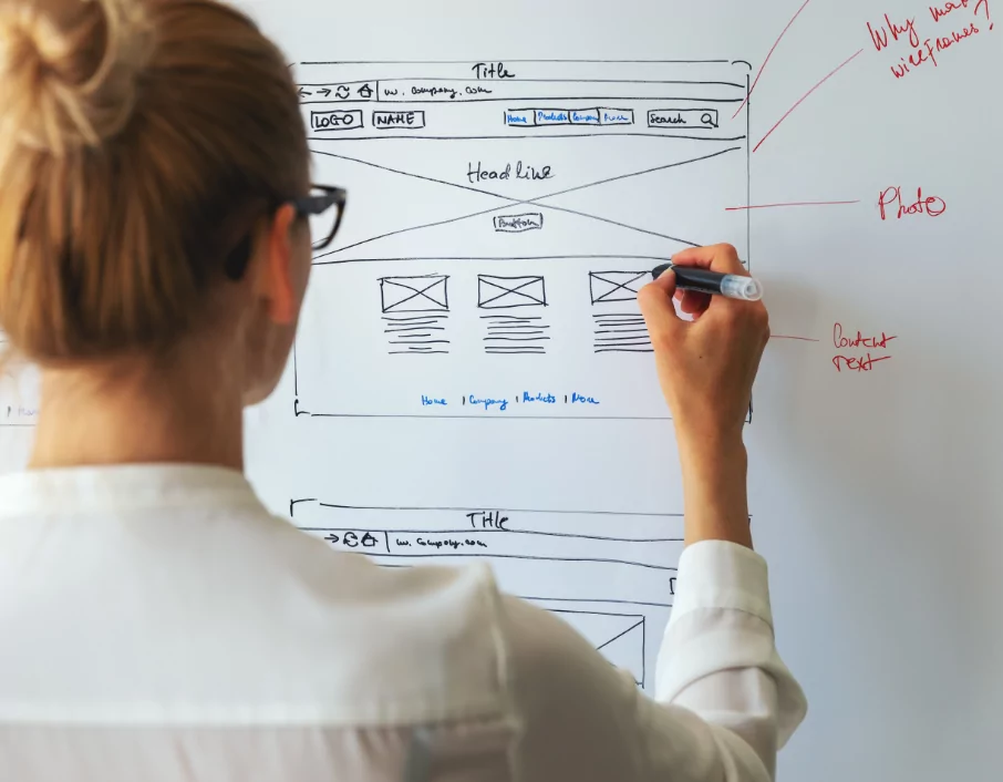 Woman designing a wireframe for a website on a whiteboard.