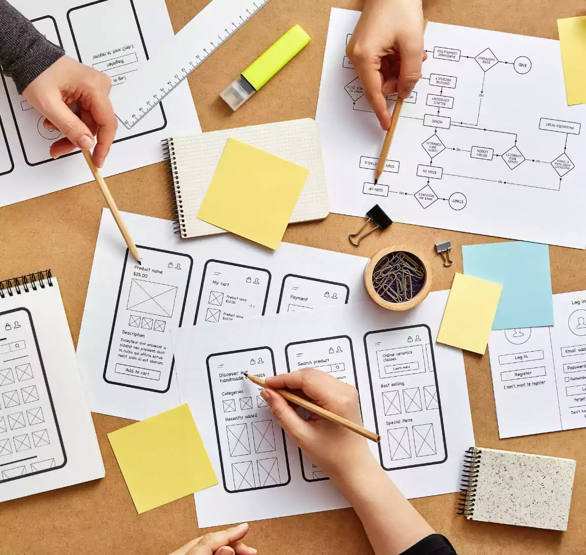 Three people are standing around a table, pointing out black and white mockups.