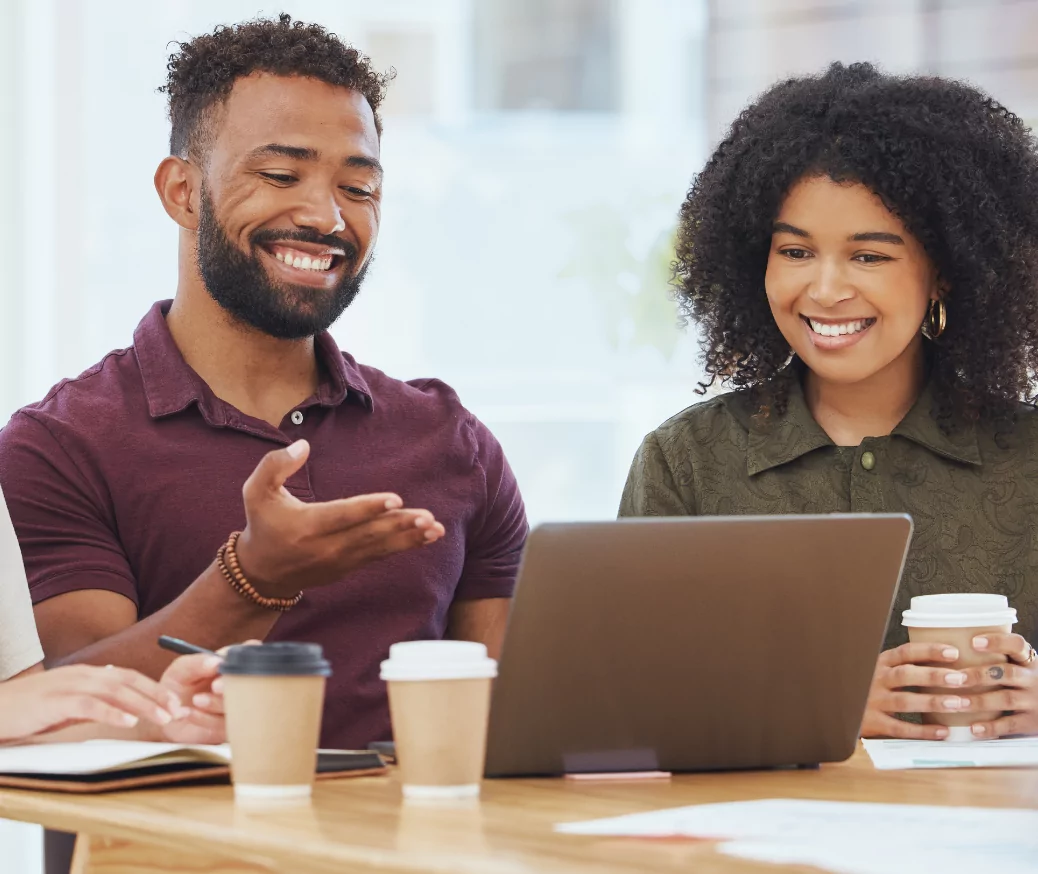 A man and woman sitting at a table reviewing a presentation on a laptop.