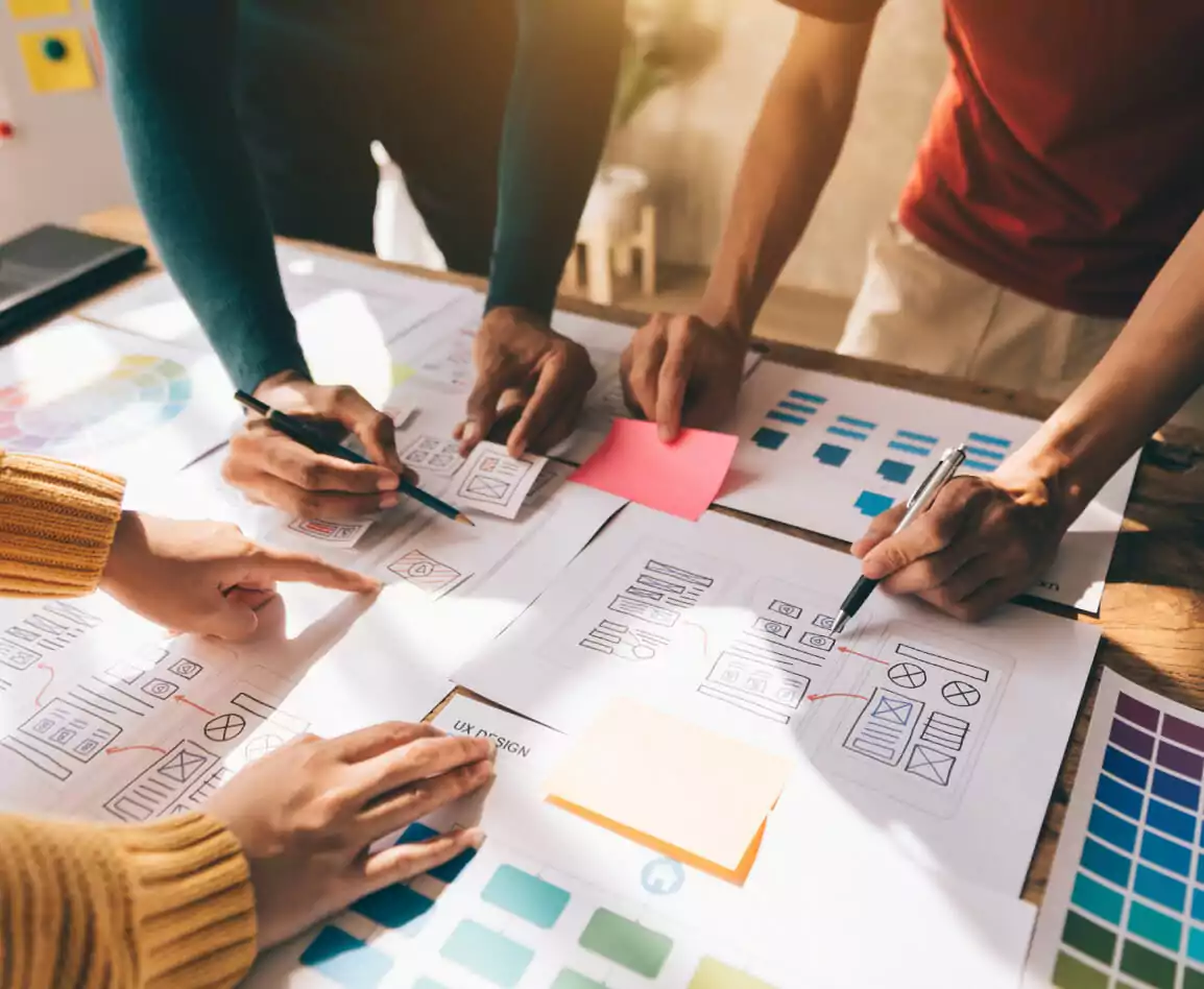 Three people gathered around a table that is filled with black and white mockups and color boards.