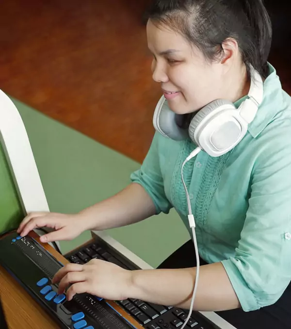 A girl using a braille keyboard in front of a computer.