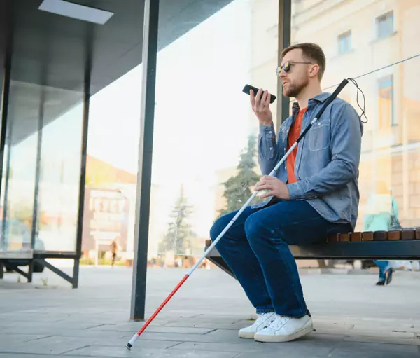 Visually impaired man sitting on a bench and talking on his phone.