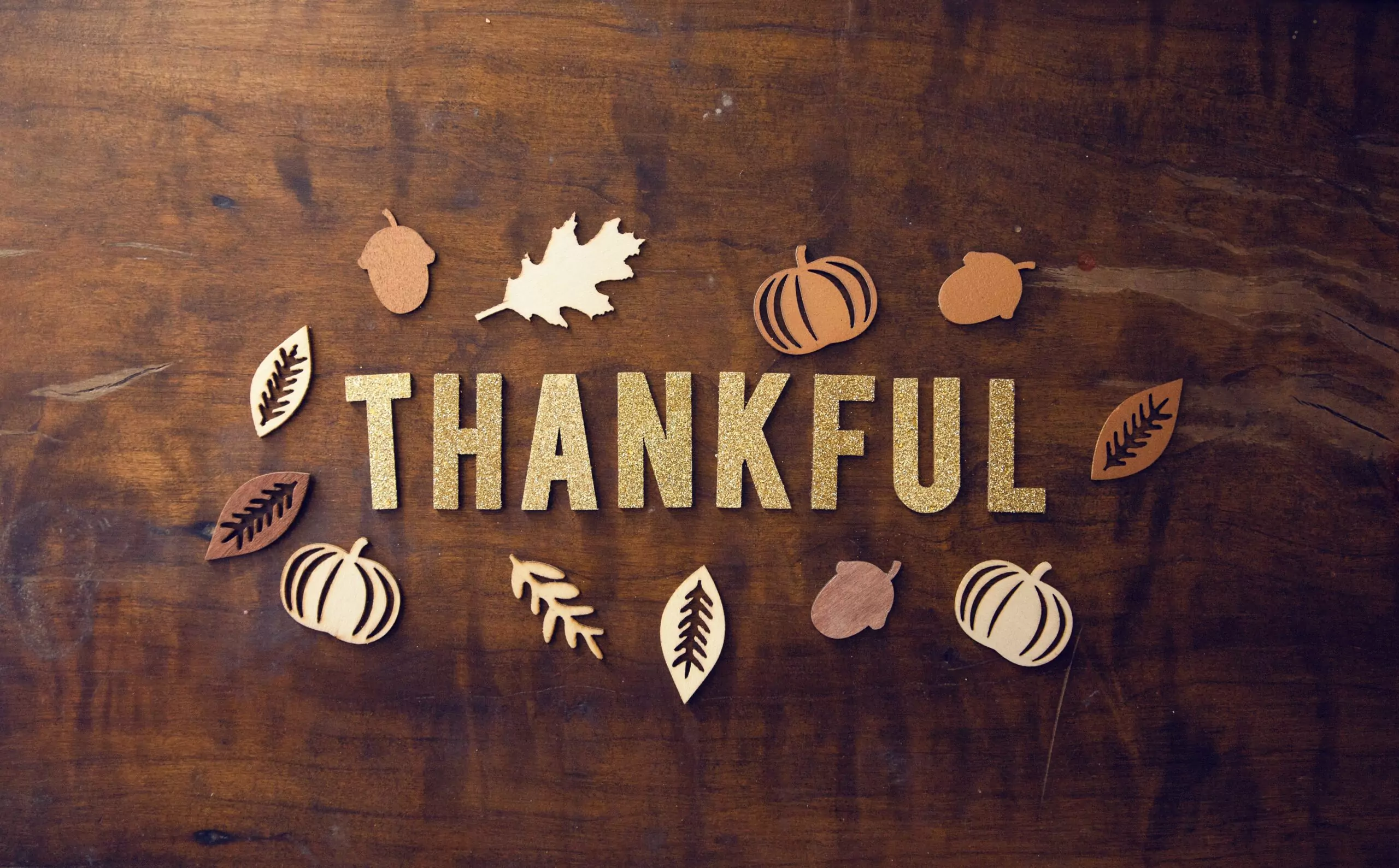 A dark wooden table with the word Thankful spelled out in tan letters. Surrounding it are various cutouts of leaves, pumpkins, acorns, and a football.